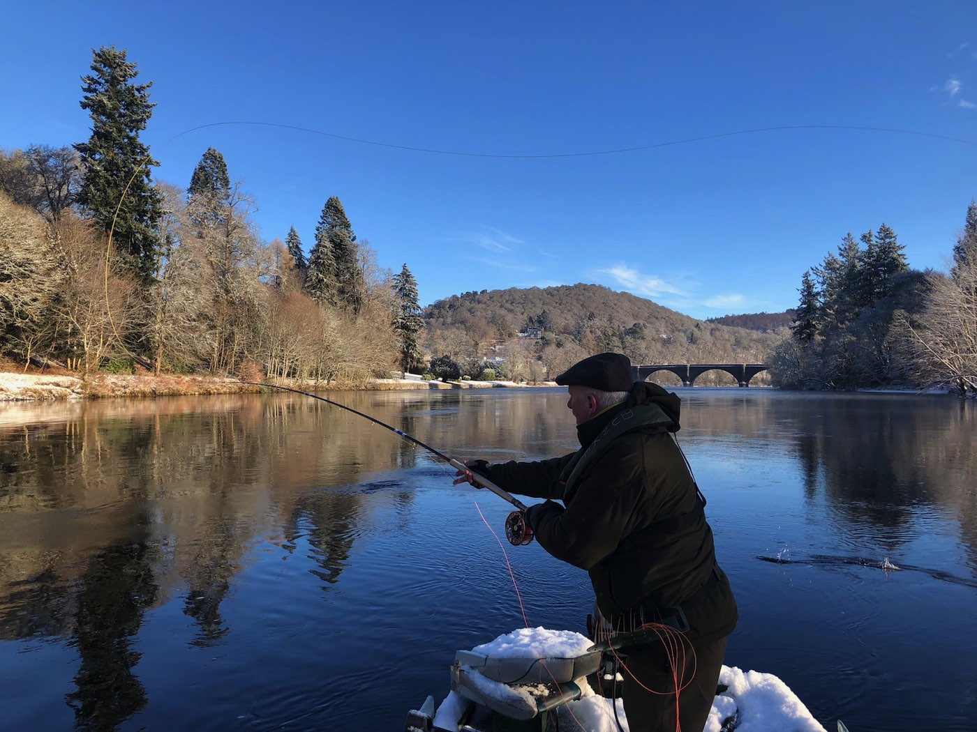 This River Tay fly fisher is Spey casting from the traditional Tay salmon fishing boat during late January on the Tay at Dunkeld. If you look closely you'll see the 200 year old Telford Bridge in the distance which is one of the Tay's most historic & beautiful sandstone bridges.