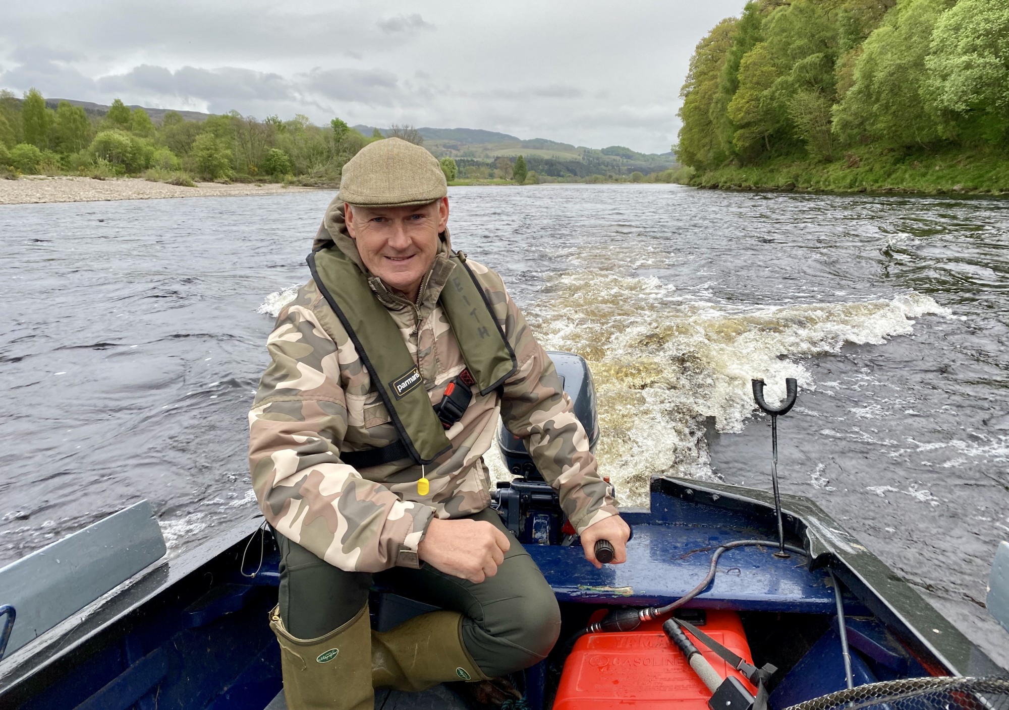 Here's Jock Monteith powering upstream in a traditional larch built River Tay salmon fishing 'coble' boat at the confluence of the River Tay & River Tummel during the month of May. Jock has his cold weather clothing on and Tweed cap in addition to his life jacket which is essential for all boat or riverbank duties.